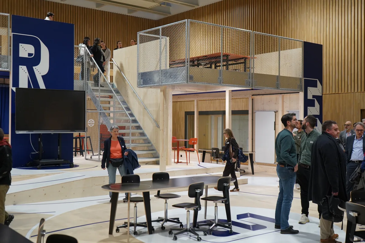 Blick in einen grossen offenen Raum. Man sieht Flächen mit Tischen und Stühlen und Aufgänge auf Emporen.